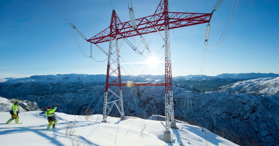 To menn på inspeksjon av en kraftmast på en snøkledd fjelltopp. Foto